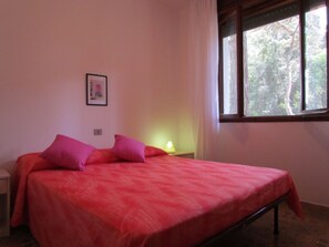 A bedroom with a single bed, a nightstand, a lamp, and a window with a view of trees.