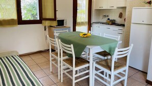 Una cocina compacta con armarios blancos, un microondas y un refrigerador. Hay una mesa de comedor con cuatro sillas y un mantel verde.
