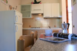 Een keuken met witte kastjes, een gasfornuis, een koffiezetapparaat en een tijdschrift op het aanrecht.