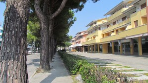 A tree-lined street with multi-story buildings, a sidewalk, and a clear sky. - Spacious Apartment With Large Balcony (San Michele al Tagliamento)