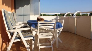 An outdoor balcony with white chairs and a table, a basket of pine cones, and a view of greenery. - Residence With Large Swimming Pool And Beach Place (San Michele al Tagliamento)