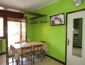 Un comedor con mesa y sillas, un reloj en la pared y una puerta que da a la cocina.