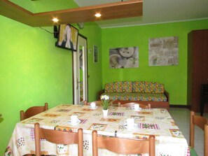 A dining area with a table set for four, chairs, a sofa, and a television mounted on the wall. - Lido Dei Pini Near Beach And Shopping Street (San Michele al Tagliamento)