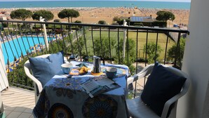 A balcony with a table set for two, overlooking a beach and a pool. - Beachfront Flat With View (San Michele al Tagliamento)