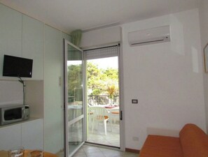 Une pièce dotée d’une porte-fenêtre coulissante donnant sur un espace extérieur, d’un téléviseur à écran plat fixé au mur et d’un four à micro-ondes posé sur le plan de travail.