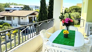 A balcony with a table set for two, surrounded by white chairs, and a vase with flowers. - Flat With Spacious Balcony in Bibione (San Michele al Tagliamento)