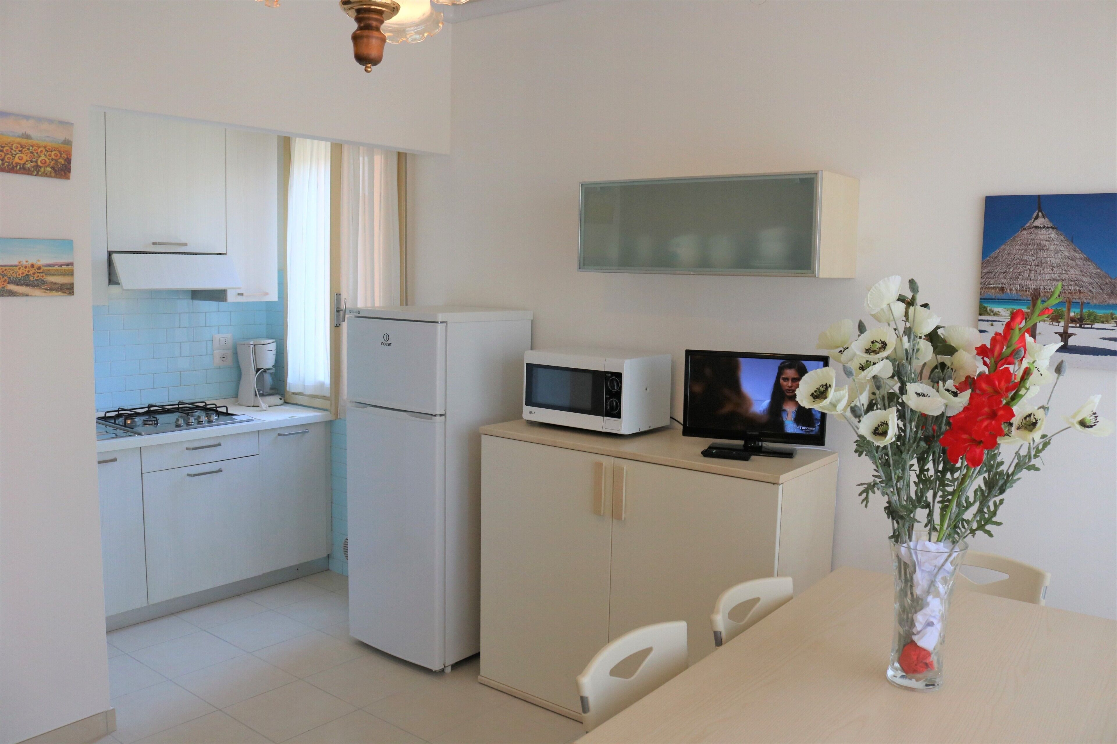 A compact kitchen with white cabinets, a microwave, a refrigerator, and a dining table with chairs.