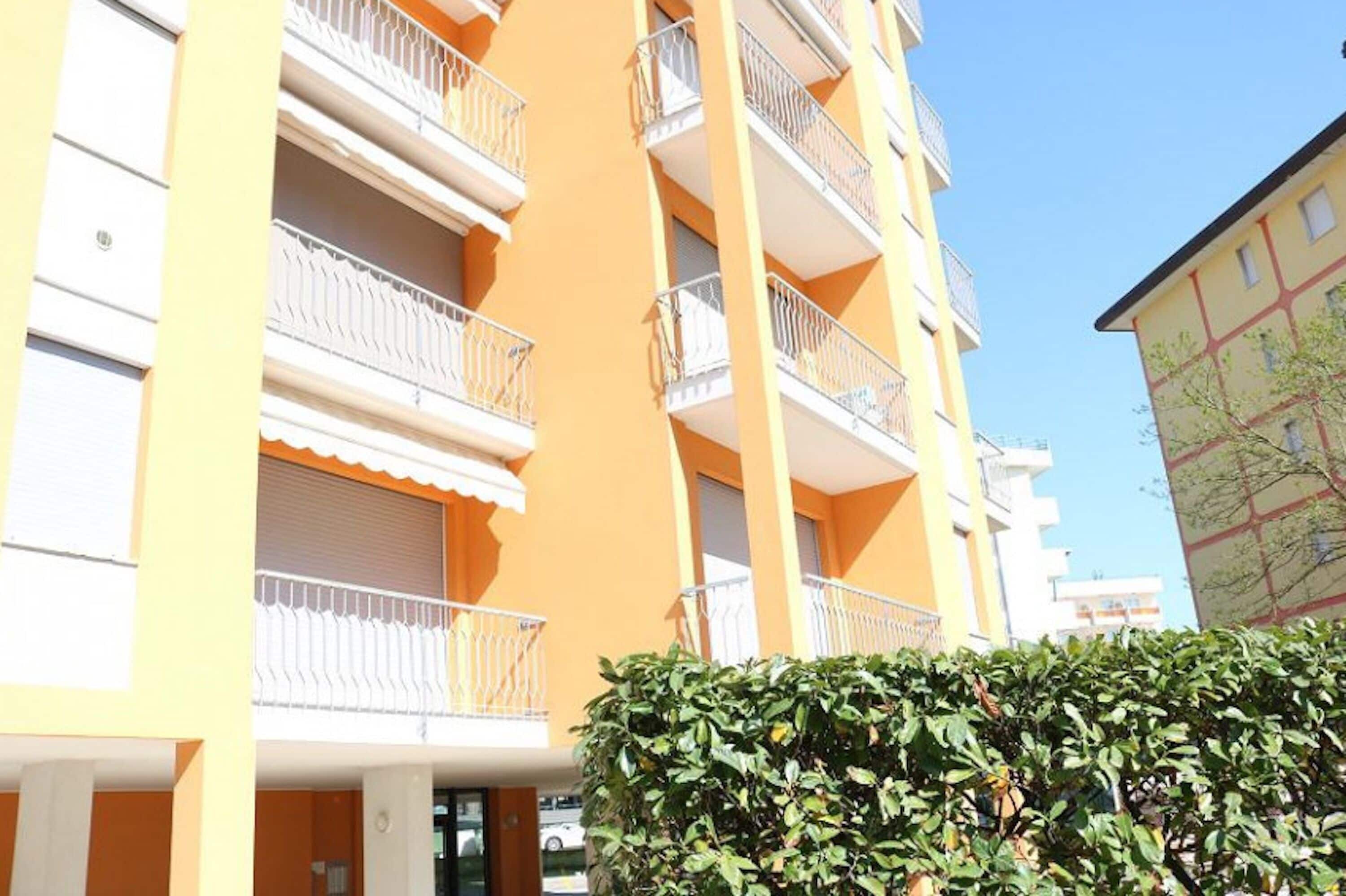 Un edificio de varios pisos con balcones, un seto en primer plano y un cielo despejado.