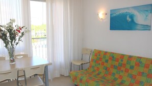 A room with a dining table, chairs, a colorful sofa, a vase with flowers, and a painting of a surfer on a wave. - Stay Just few Meters From the Beach (San Michele al Tagliamento)