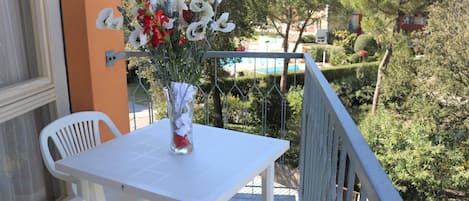 Ein Balkon mit weißem Tisch und Stühlen, einem Blumenstrauß und Blick auf Pool und Grünflächen.