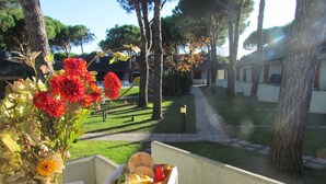 Uma mesa com um vaso de flores e um tabuleiro de comida, com um jardim bem cuidado e uma fileira de edifícios ao fundo.
