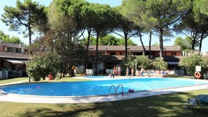 Piscina com escorrega, rodeada por árvores e um edifício com várias varandas.