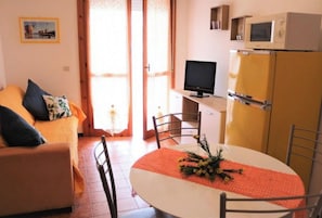 A compact living space with a sofa, a dining table with a flower centerpiece, a television, and a refrigerator.