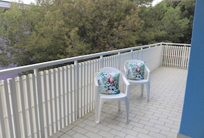 A balcony with two white chairs, a white picket fence, and a view of trees.