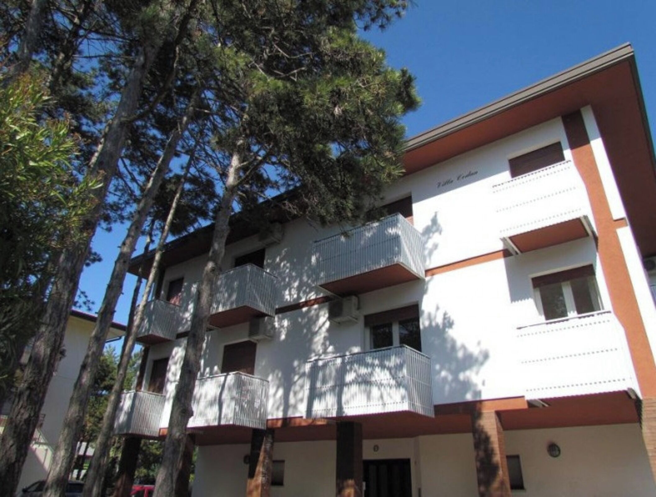 A multi-story building with balconies, surrounded by tall trees.