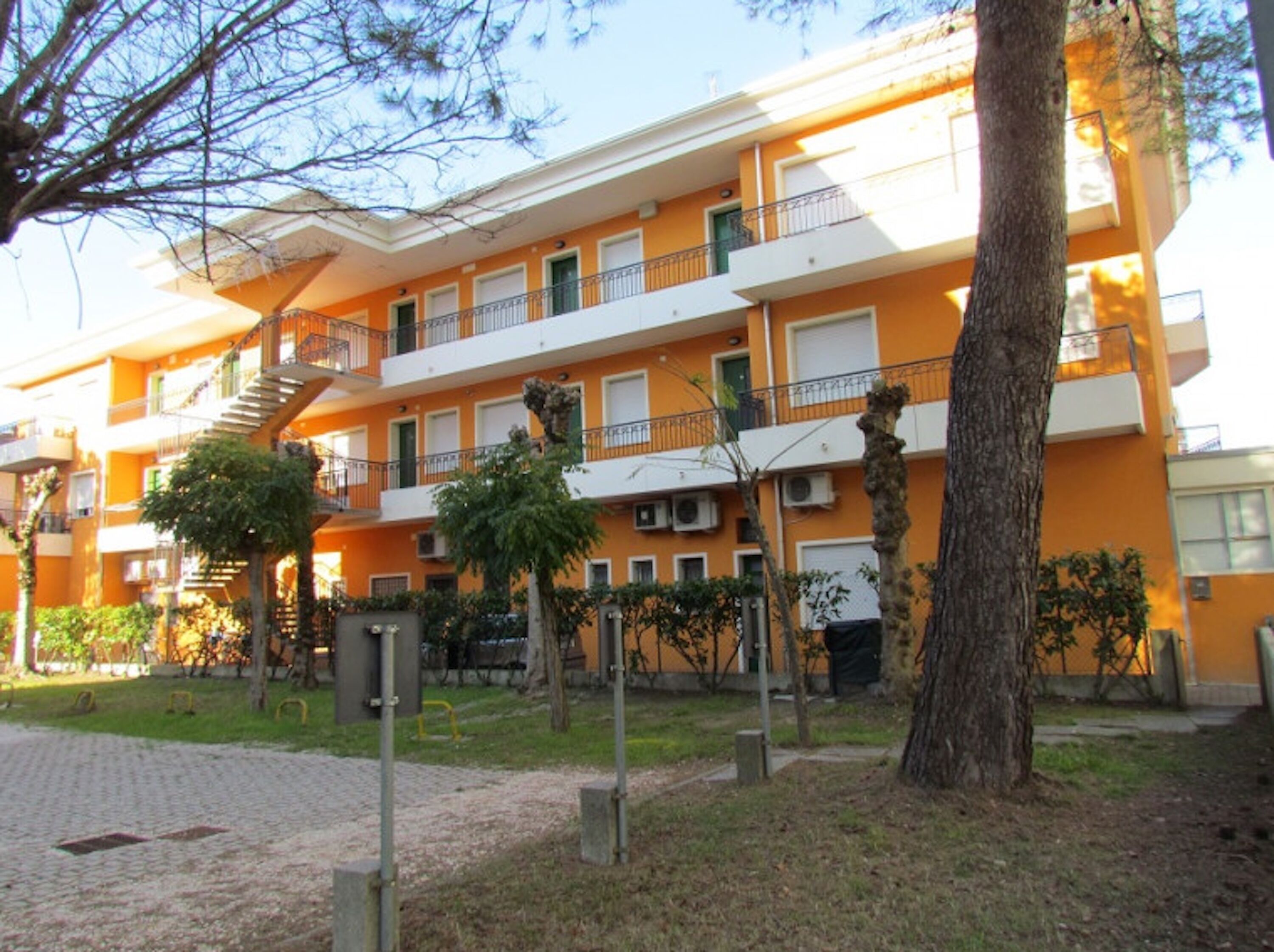 A multi-story building with balconies, a staircase, and a courtyard with trees and a brick pathway.