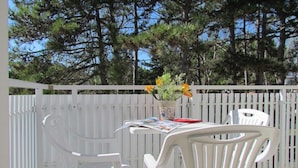 Ein weißer Außenbereich mit Tisch und Stühlen, einem weißen Zaun und einem Blumentopf mit gelben Blüten.