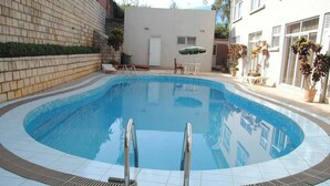 A swimming pool with two ladders, a small table with chairs, and potted plants.