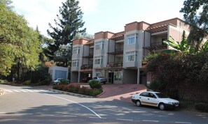 A multi-story residential building with balconies, a parking area, and a street in front. - Room-wonderful Kigali Double Room (Kigali)