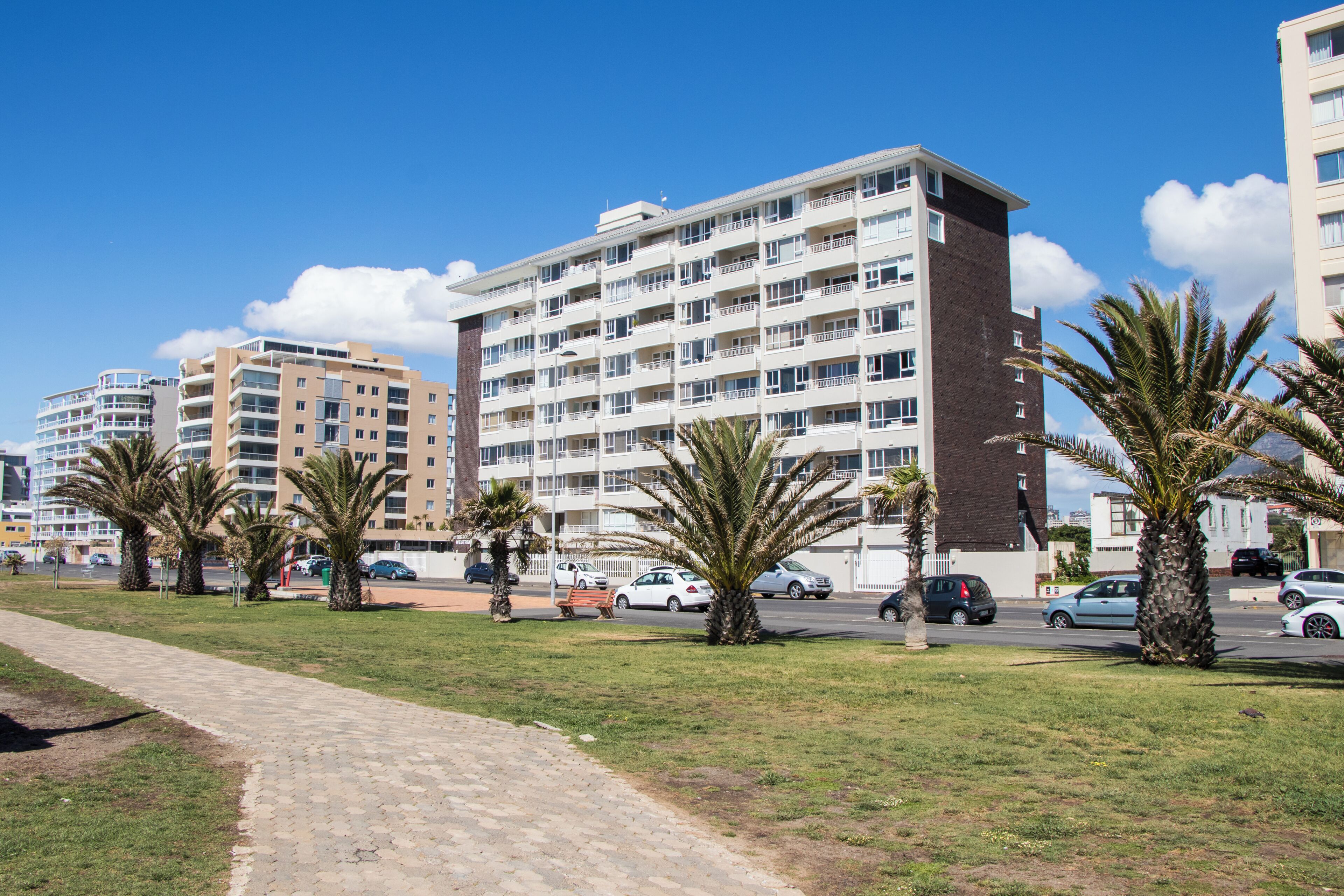 A multi-story hotel with a brick facade, multiple balconies, and a paved walkway with palm trees.