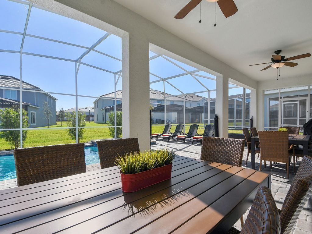 A covered patio with a pool, wicker furniture, and a ceiling fan.