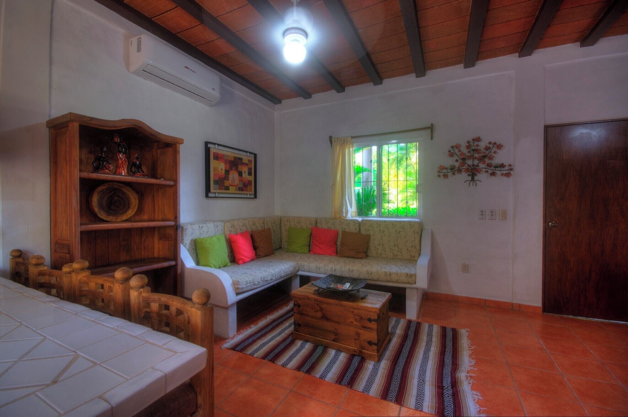 Un salón acogedor con sofá, aparador de madera y ventana con vistas a la vegetación.