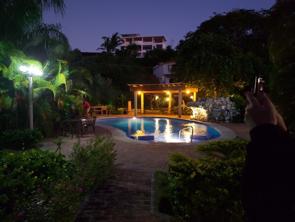 A swimming pool surrounded by lush greenery and a gazebo. - Bungalows Las Margaritas 2 (Higuera Blanca)