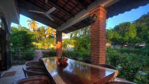 An outdoor dining area with a long wooden table and leather chairs, surrounded by lush greenery and palm trees. - Bungalows Las Margaritas 2 (Higuera Blanca)