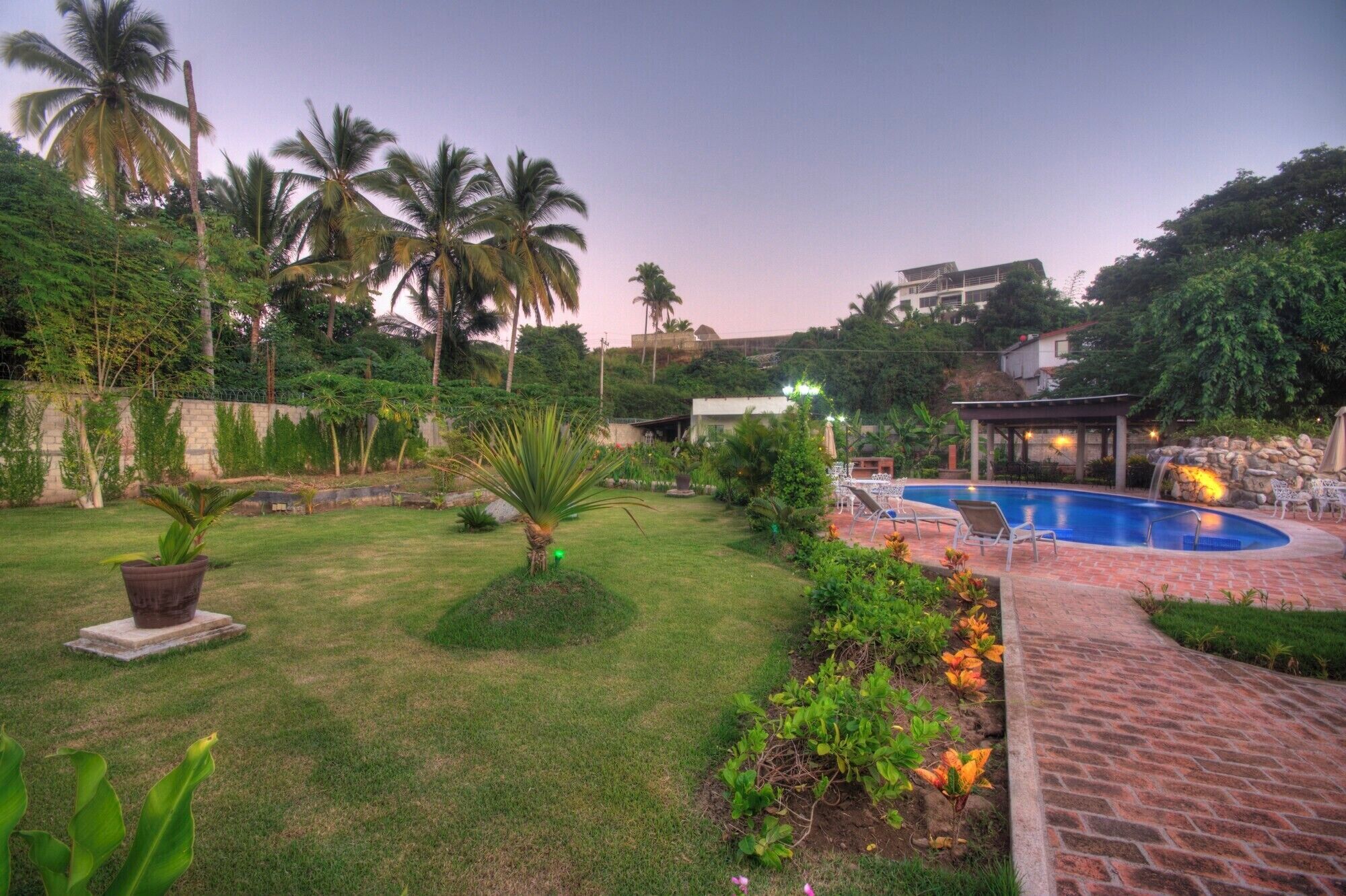 A pool area with a brick pathway, lounge chairs, and a gazebo.