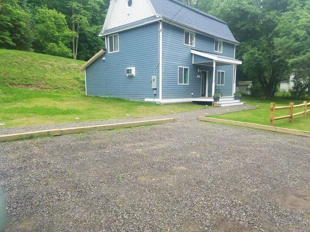 A two-story house with a porch, a gravel driveway, and a wooden fence.