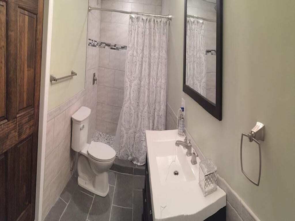 A bathroom with a toilet, shower, sink, and mirror.
