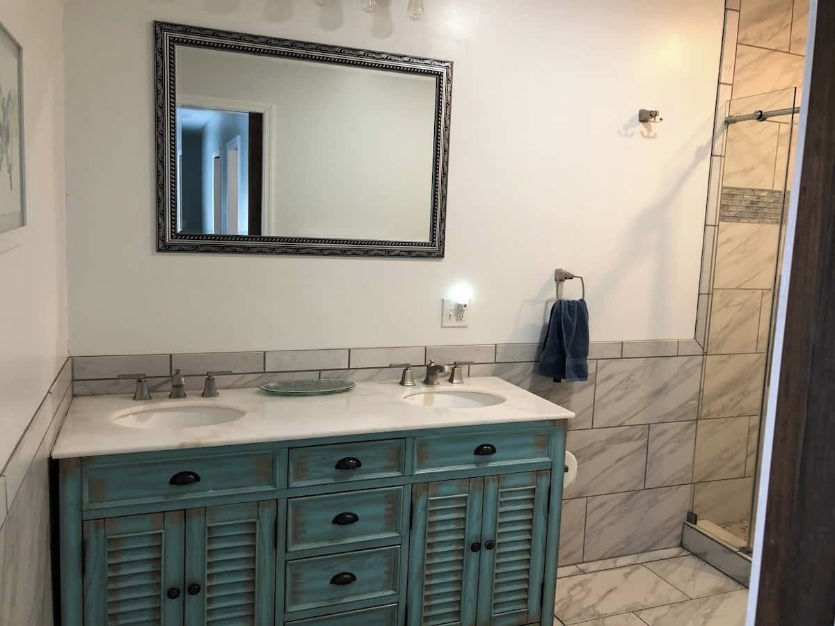 A bathroom with two sinks, a mirror, and a shower.