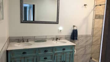 A bathroom with two sinks, a mirror, and a shower.