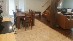 Un coin repas avec une table et des chaises en bois, une cuisine équipée d’une cuisinière et un escalier menant à un espace de vie agrémenté d’un canapé en cuir.