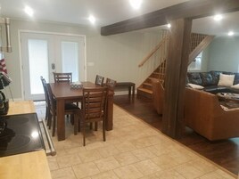 Un comedor con mesa y sillas de madera, una cocina con estufa, y una escalera que lleva a una sala de estar con sofá de cuero.
