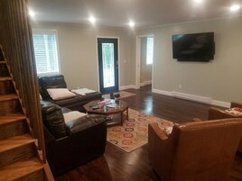 Una sala de estar con una escalera, sofás de cuero, una mesa de centro y un televisor montado en la pared.