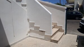 Eine weiße Treppe führt zu einer oberen Ebene, ein geparktes Auto und ein Gebäude mit weißer Fassade.