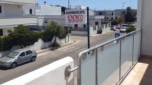 Blick auf eine Straße mit einem Supermarktschild, einem am Straßenrand geparkten Auto und Gebäuden im Hintergrund.