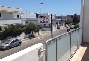 Une vue d’une rue avec une enseigne de supermarché, une voiture garée sur le bord et des bâtiments en arrière-plan.