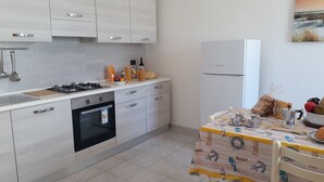Eine moderne Küche mit Herd, Backofen und Kühlschrank. Ein Esstisch mit bunten Tischdecken und verschiedenen Küchenutensilien steht daneben.