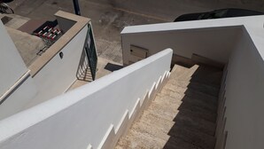 A staircase leading to a rooftop area with a white railing, a metal gate, and a small enclosed space with a trash bin.