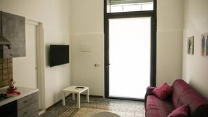 A small, compact living space with a kitchenette, a sofa, a small table, and a sliding glass door leading to a balcony. - Palazzo Nicastro Guest House Red (Avola)