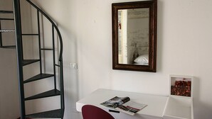 A room with a white desk, a red chair, a spiral staircase, and a mirror on the wall. - Palazzo Nicastro Guest House Red (Avola)