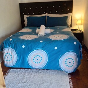 Ein Bett mit einer blau-weißen Bettdecke, ein weißes Handtuch und ein grauer Teppich.