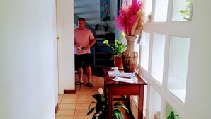 A hallway with a tiled floor, a wooden table with a vase and a plant, and a door leading to another room.