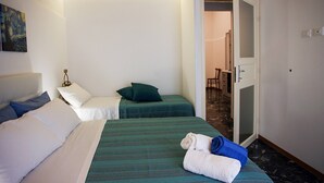A hotel room with two beds, one with white bedding and the other with green bedding. There are towels on the bed and a painting on the wall. - Palazzo Nicastro Guest House Blue (Avola)