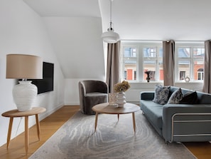 Uma sala de estar moderna com sofá, poltrona, abajur e vista para edifícios pela janela.