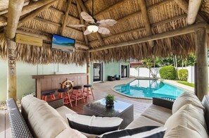 Un espace aménagé au bord de la piscine, doté d’un toit de chaume, d’un bar avec des tabourets et d’un canapé.