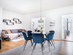 Uma sala de estar moderna com sofá, mesa de jantar com cadeiras, luminária pendente e obras de arte nas paredes.