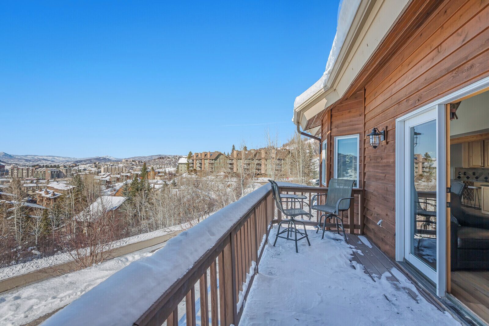 A balcony with a view of a snowy town, wooden railing, and a table with chairs.